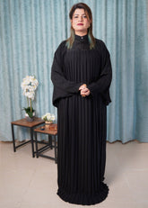 Woman wearing a black dress standing in a room with light blue curtains and a small table with flowers.