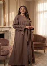 Woman in a long brown dress standing in a room with beige walls and a fireplace.