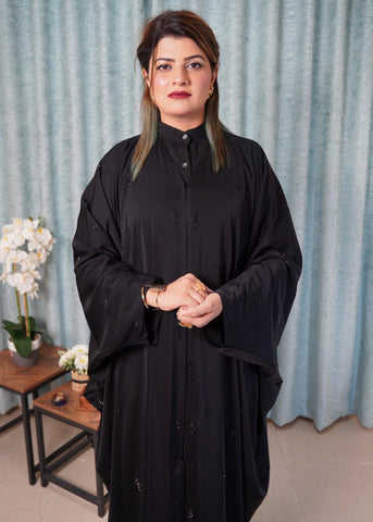 Woman wearing a black outfit standing in a room with light blue curtains and a small table with flowers.