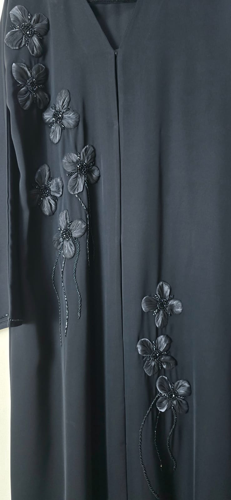 A dark charcoal gray abaya featuring intricate black floral embroidery and beadwork along the front panels and sleeves.