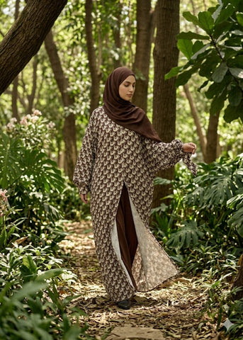 Modest woman wearing a printed brown CrepeLoom and Farasha 3-piece abaya set with ribbon sleeves and matching CrepeLoom hijab in a forest setting.
