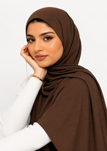 Woman wearing a brown liquid jersey hijab and white sweater against a plain background