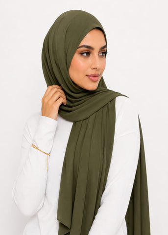 Woman wearing an olive green liquid jersey hijab and white outfit on a light gray background