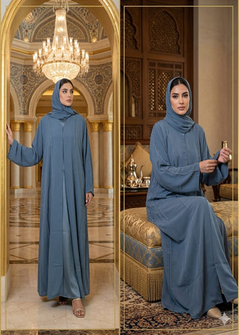 Woman in a blue abaya standing in an ornate room with chandelier and decorative elements.