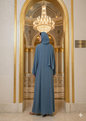 Person wearing a blue abaya standing in front of a grand mirror with a chandelier above.